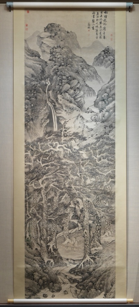 Paisaje vertical denso de pinos y rocas en tinta sobre papel, con un ermitaño tocando la cítara; foto con el montaje completo del rollo.